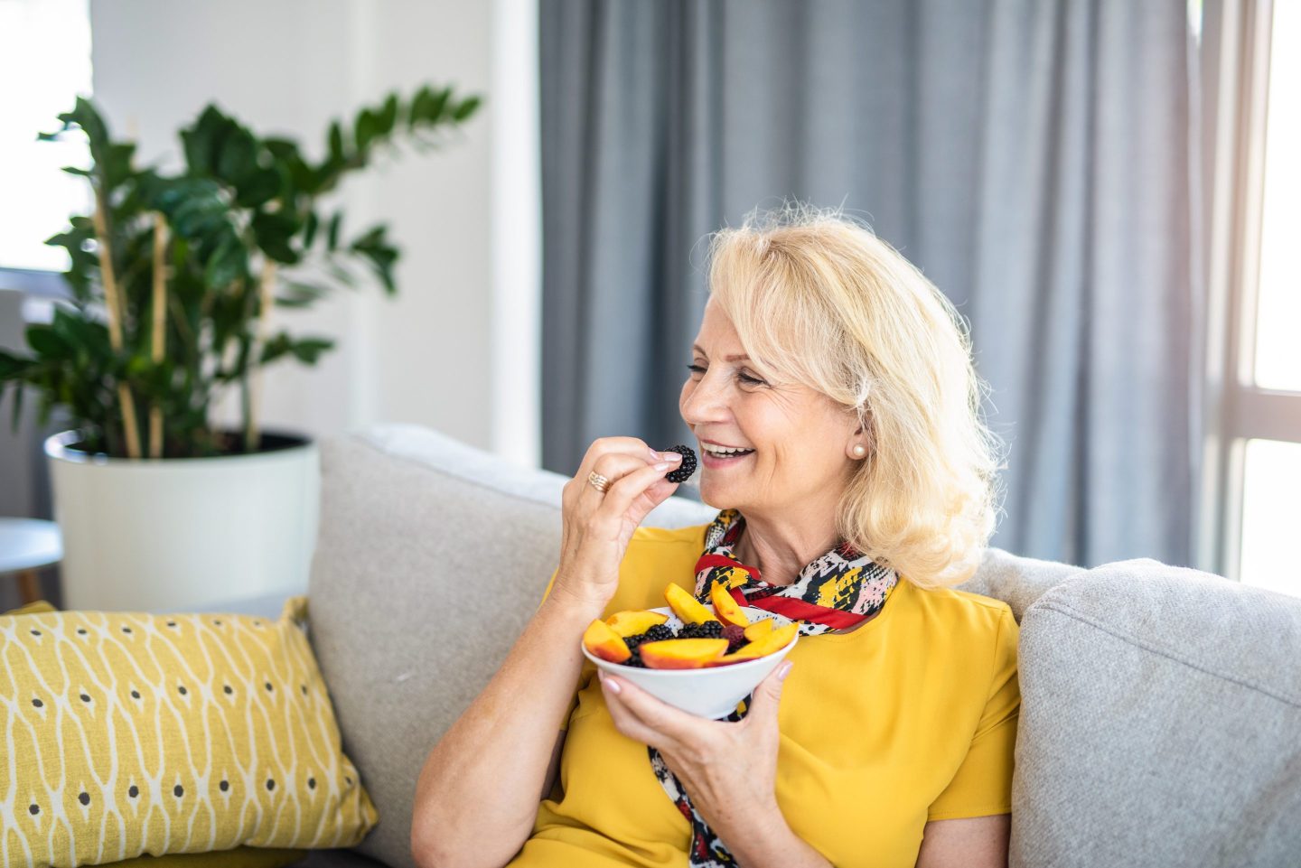 Healthy senior woman eating healthy fruit salad in the living room.